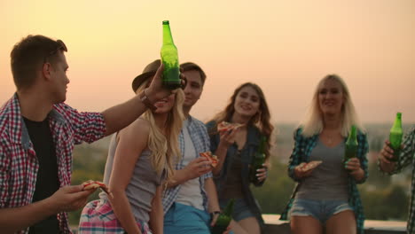 A-boy-raises-a-toast-to-a-friend's-birthday-in-friends-company-on-the-roof.-They-clink-beer-and-eat-pizza.